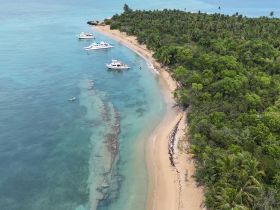 A stunning aerial view of a serene beach with multiple boats anchored along the coastline, surrounded by lush greenery — a perfect destination for relaxation and exploration.