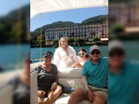 A joyful family enjoys a sunny day on a boat, capturing memories with smiles and laughter against a picturesque backdrop of mountains and waterfront buildings.