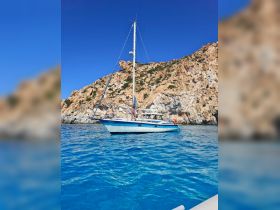 A couple enjoys a scenic day on their sailboat, surrounded by stunning rocky cliffs and crystal-clear waters, perfect for a memorable sailing adventure.