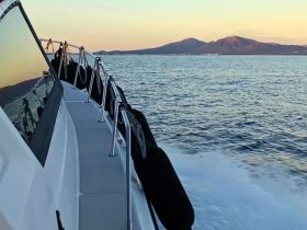 A sleek boat cruising through calm waters, showcasing its elegant profile against a backdrop of distant mountains at sunset.