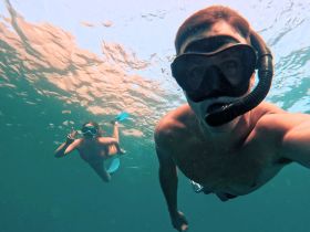 A couple enjoys snorkeling underwater, capturing a fun moment while exploring the vibrant marine life — perfect for adventure seekers.