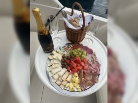 A beautifully arranged charcuterie platter with assorted cheeses, meats, and fresh fruits, paired with champagne — perfect for a luxurious day on the water.