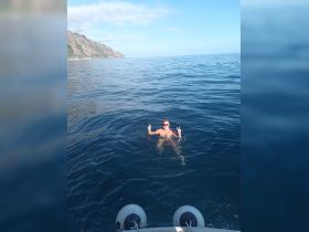 A joyful swimmer poses with peace signs in the serene ocean, showcasing a fun day on the water surrounded by stunning coastal views.
