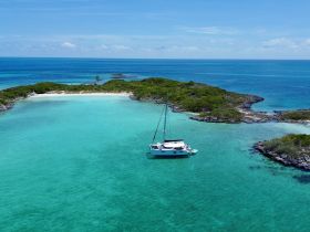 A stunning aerial view of a catamaran anchored in crystal-clear turquoise waters, surrounded by lush greenery and a serene beach — perfect for a tropical getaway.