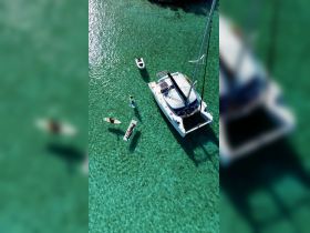 Aerial view of a lively group enjoying paddleboarding and snorkeling around a catamaran in crystal-clear waters, perfect for a fun day on the water.