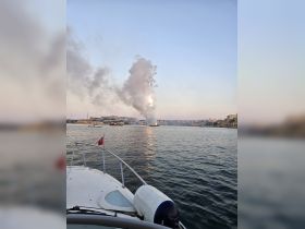 A scenic view from a boat capturing smoke rising in the distance, reflecting the beauty of the water and the sunset — perfect for those seeking picturesque moments on the water.
