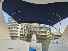 A man stands at the helm of a boat, enjoying the view of waterfront buildings — a perfect setting for relaxation and exploration on the water.