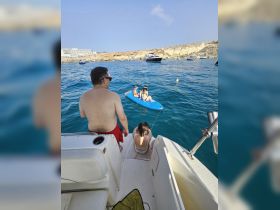 A family enjoys a fun day on the water, with kids paddleboarding while adults relax on the boat — perfect for summer adventures and family bonding.