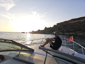 A man relaxes on the bow of a boat during a stunning sunset, capturing the essence of tranquil evenings on the water.