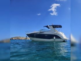 A stunning side view of a yacht cruising through clear waters, showcasing its sleek design against a backdrop of a rocky island under a bright blue sky.
