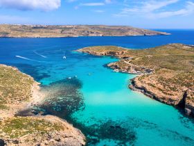 A stunning aerial view of a turquoise bay surrounded by rugged coastline, showcasing the natural beauty of the area — perfect for exploring by boat.