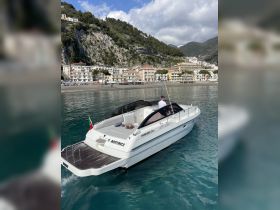 A sleek Pershing 33 speedboat glides through clear waters, showcasing its elegant design against a stunning coastal backdrop.