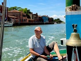 A man relaxes on a boat while navigating through a picturesque canal, surrounded by charming waterfront buildings — a perfect scene for exploring scenic waterways.