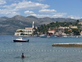 A picturesque view of a coastal town with a boat anchored in the foreground and a person enjoying the water, showcasing the beauty of summer days by the sea.