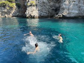A group of friends enjoys a refreshing swim in crystal-clear waters near stunning cliffs, capturing the essence of summer adventures on the water.