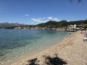 A picturesque beach scene with clear waters and people enjoying the sun and swimming, set against a backdrop of charming coastal town and mountains.