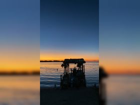 A serene sunset view from a dock with a person swimming nearby, creating a picturesque scene perfect for evening relaxation and water activities.
