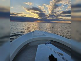 A serene view from the front of a boat as it glides through calm waters at sunset, showcasing the beautiful sky and tranquil atmosphere.