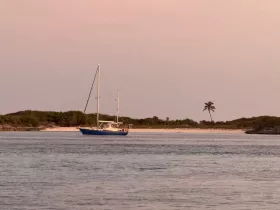 A serene view of a sailboat anchored near a sandy beach, surrounded by lush greenery and a tranquil atmosphere, perfect for sailing enthusiasts and nature lovers.