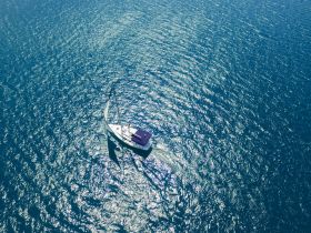 A stunning aerial view of a sailboat gliding through sparkling blue waters, perfect for showcasing sailing adventures and maritime beauty.