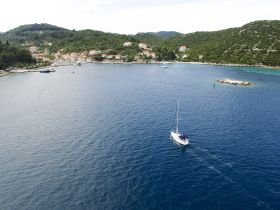 An aerial view of a sailboat navigating through tranquil waters, surrounded by lush hills and a picturesque coastal village — perfect for showcasing sailing adventures.