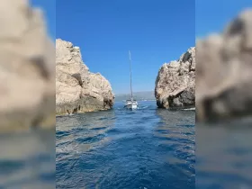 A sailboat navigates through a stunning rock formation, showcasing the beautiful coastline and clear blue waters — a perfect scene for adventure seekers.