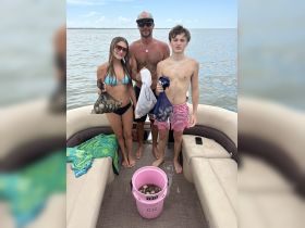 A family enjoys a fun day of clam digging on a pontoon boat, showcasing their catch in a YETI bucket — a perfect summer adventure on the water.
