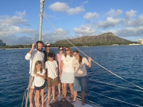 A joyful family poses together on a sailboat with a stunning ocean backdrop and a mountain view, capturing a memorable moment during their boating adventure.