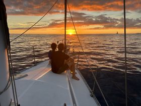 A serene sunset view from a sailboat, featuring a couple enjoying the moment together — an ideal setting for romantic sailing trips.