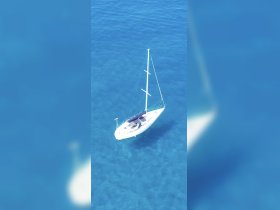 Aerial view of a sleek sailboat gliding through crystal-clear waters, perfect for sailing enthusiasts and adventure seekers.