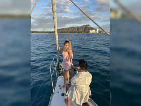 A couple enjoys a romantic moment aboard a sailboat, with stunning ocean views and a picturesque backdrop of Diamond Head, perfect for proposals and special occasions.