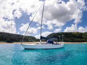 A beautiful sailboat anchored in crystal-clear turquoise waters, surrounded by lush greenery and a sandy beach — perfect for a relaxing day on the water.