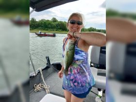A joyful angler proudly displays her catch of the day, a large bass, while enjoying a fishing trip on the water. Perfect for showcasing fishing adventures and outdoor fun.