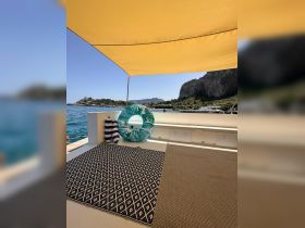 A cozy seating area on a boat featuring a stylish rug and a floating mat, perfect for relaxing under the sun while enjoying the beautiful coastal views.