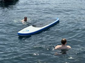 Two individuals enjoy a refreshing swim near a paddleboard, showcasing the fun of on-water activities during a sunny day.