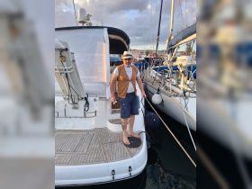 A man stands on the deck of a boat at the marina, showcasing a relaxed boating lifestyle. Perfect for capturing moments of leisure and adventure on the water.
