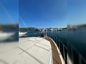 A woman stands on the deck of a yacht at a marina, enjoying the sunny day surrounded by other boats — a perfect setting for a relaxing getaway.