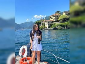 A woman celebrates on the deck of a boat, holding a bottle of champagne against a stunning lakeside backdrop — perfect for memorable outings and special occasions.