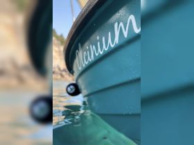 Close-up shot of the hull of a boat named 'Olcinium', showcasing its vibrant color and sleek design against a serene water backdrop.