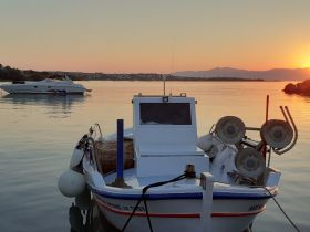 A serene view of a boat docked at sunset, with another vessel in the background, capturing the tranquility of the water and the beauty of the evening sky.