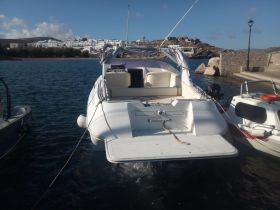 A sleek yacht is docked, showcasing its elegant design against a picturesque backdrop of white buildings and rocky terrain, perfect for exploring coastal destinations.