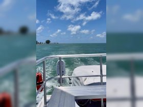 A scenic view from the back of a boat cruising through turquoise waters, showcasing the beautiful shoreline and clear blue skies.