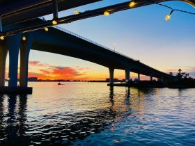 A stunning sunset view under a bridge, reflecting on the water, creating a picturesque scene perfect for evening boat rides.