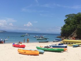 A vibrant beach scene with people enjoying various water activities, including kayaking and boating, set against a backdrop of clear blue skies and calm waters.