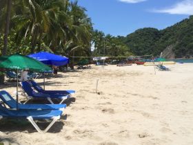 A sunny beach scene featuring lounge chairs and umbrellas, with some people in the background enjoying the tropical setting.