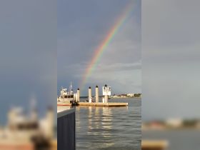 A vibrant rainbow arcs over a dock with a gas station, creating a picturesque scene perfect for boating enthusiasts and nature lovers.