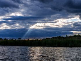 A stunning view of dramatic clouds and sunlight breaking through over tranquil waters, capturing the serene beauty of nature — perfect for nature lovers and photographers.