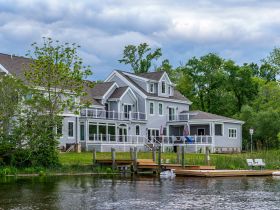 A scenic view of a lakeside house with a dock, surrounded by greenery. The image captures the tranquil atmosphere of waterfront living.