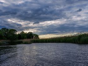 A serene view of a calm waterway under a dramatic sky, showcasing the beauty of nature and perfect for peaceful boat outings.