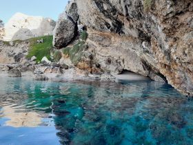 A serene view of a secluded beach surrounded by rocky cliffs and crystal-clear waters, perfect for exploring hidden gems during a boat trip.